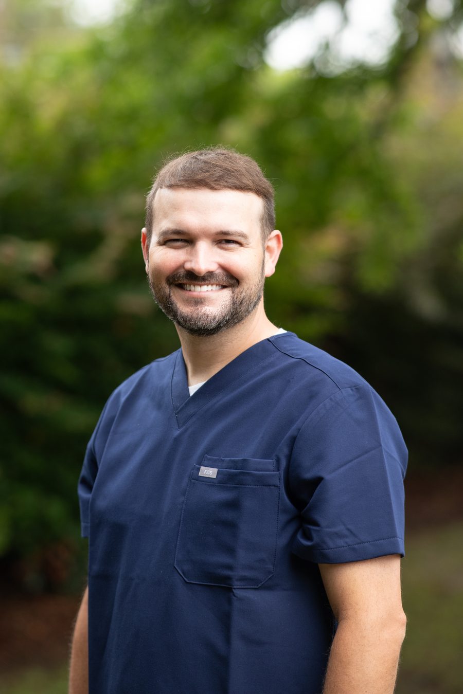 Dr. Joseph McDaniels smiling outdoors in navy scrubs