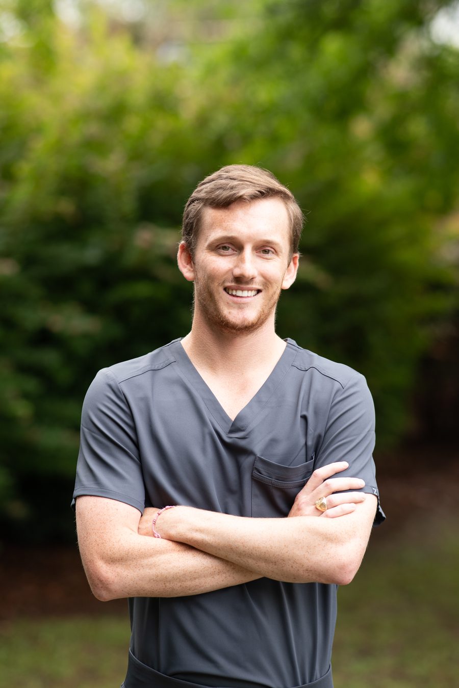 Dr. Hampton Scott smiling outdoors in gray scrubs with arms crossed